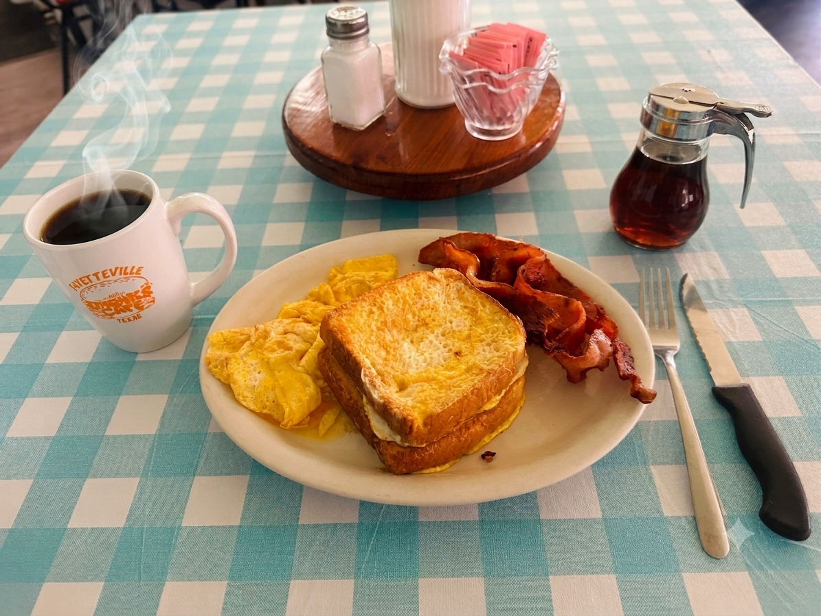 French toast, eggs, and bacon with a hot cup of coffee on a blue checkered tablecloth